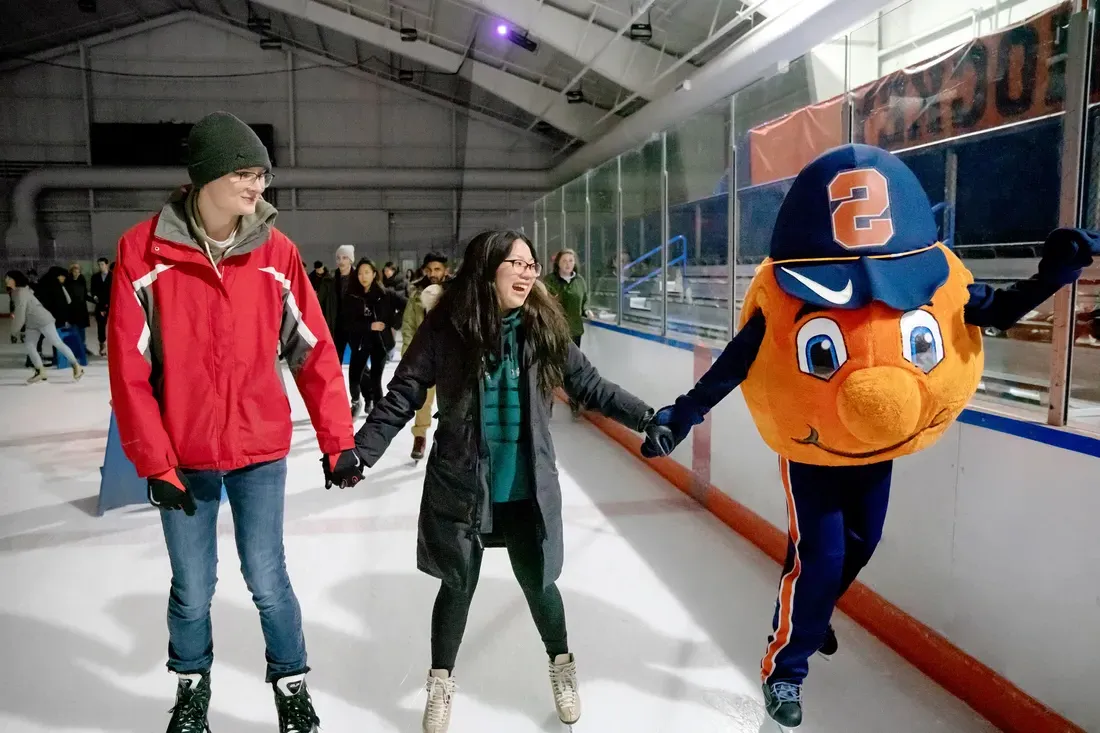 Otto ice skating with two students, all holding h和s.